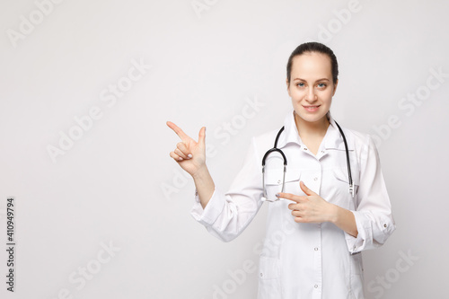 A young nurse looks at the camera and shows something on a white isolated background.