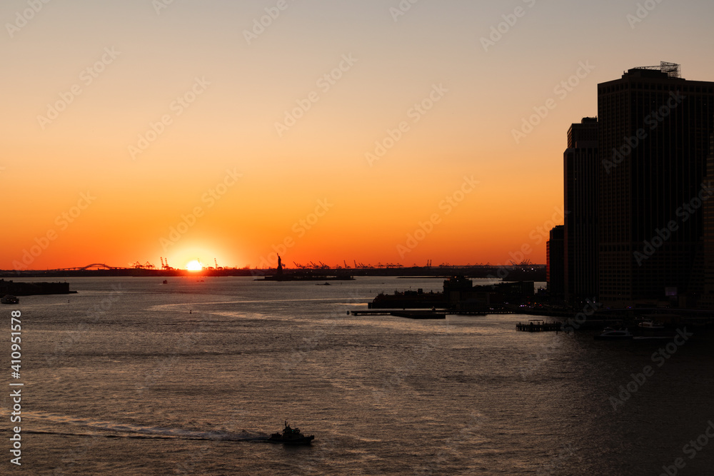 Beautiful Sunset on the East River in New York City with the Silhouette of the Statue of Liberty in the Distance and Skyscrapers