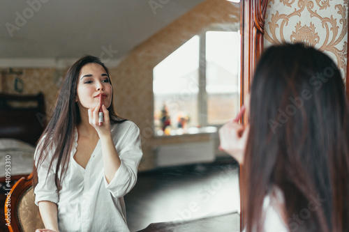 Girl paints her lips in front of the mirror, puts lipstick on her lips in her room