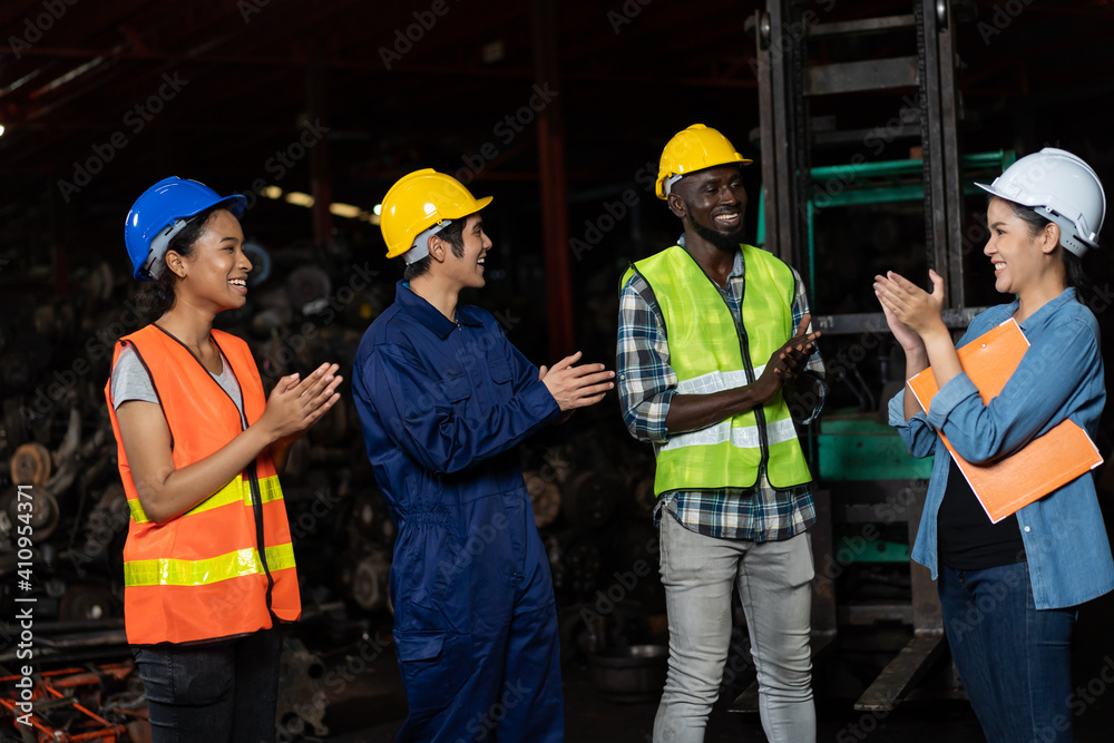 Happy group of diversity factory worker greeting about work at old garage parts storage warehouse. Group of factory worker successful meeting and wearing safety vest and helmet