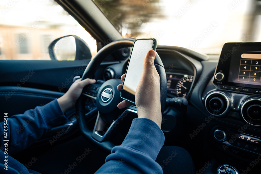 Teen drive a car and use smartphone. Young man reading messages holding a cell phone while driving. Dangerous behavior, accident risk. Danger, transgression, youth, distraction concept. Focus on hand. Teen drive a car and use smartphone. Young man reading messages holding a cell phone while driving. Dangerous behavior, accident risk. Danger, transgression, youth, distraction concept. Focus on hand.