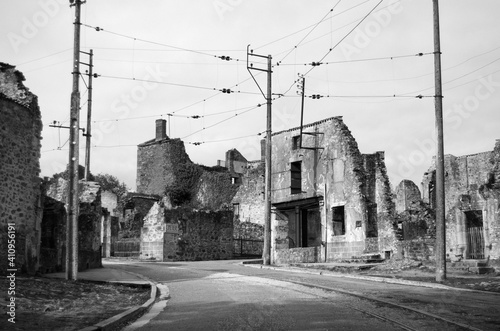 Aftermath of war shows ruined buildings and tram lines in Oradour-sur-Glane in France. This historic village is now a memorial to those who died in WW2. Monochrome image. Empty road with tram lines.