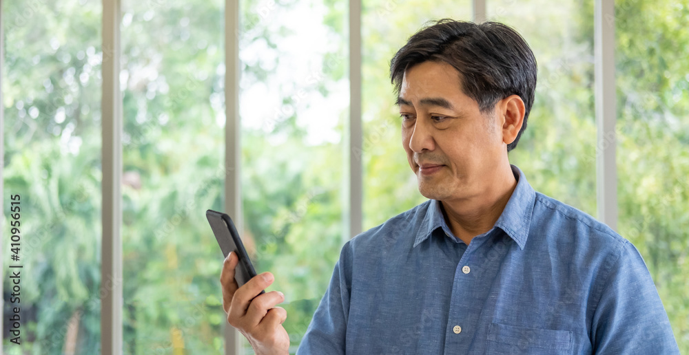 ฺBanner shot, Senior Asian man holding Smartphone in his hand while using high speed mobile internet for watching online video streaming service or news from the device. Active senior with technology. ฺBanner shot, Senior Asian man holding Smartphone in his hand while using high speed mobile internet for watching online video streaming service or news from the device. Active senior with technology.