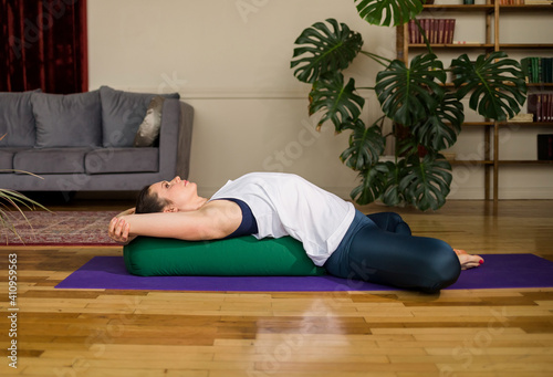 yoga woman in sportswear relaxes on bolster mat in the room