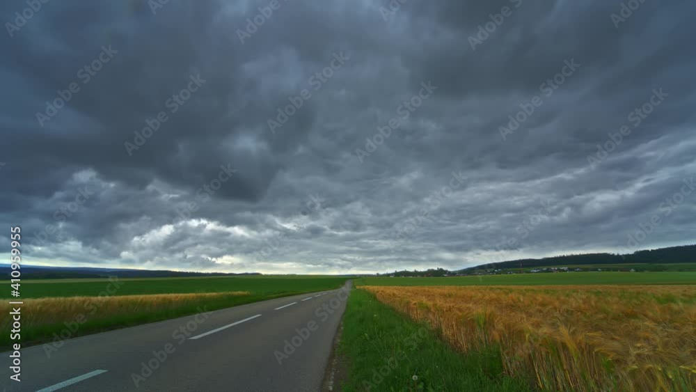 Time-lapse, rolling dark clouds in the sky, a road leading to the distance, rural scenery on cloudy day Time-lapse, rolling dark clouds in the sky, a road leading to the distance, rural scenery on cloudy day