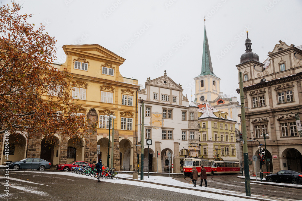 Fototapeta premium Renaissance Sternberg Palace and spire of baroque Church of St. Tomas at Lesser Town Square, Malostranske namesti, snow in winter day, Mala Strana district, Prague, Czech Republic