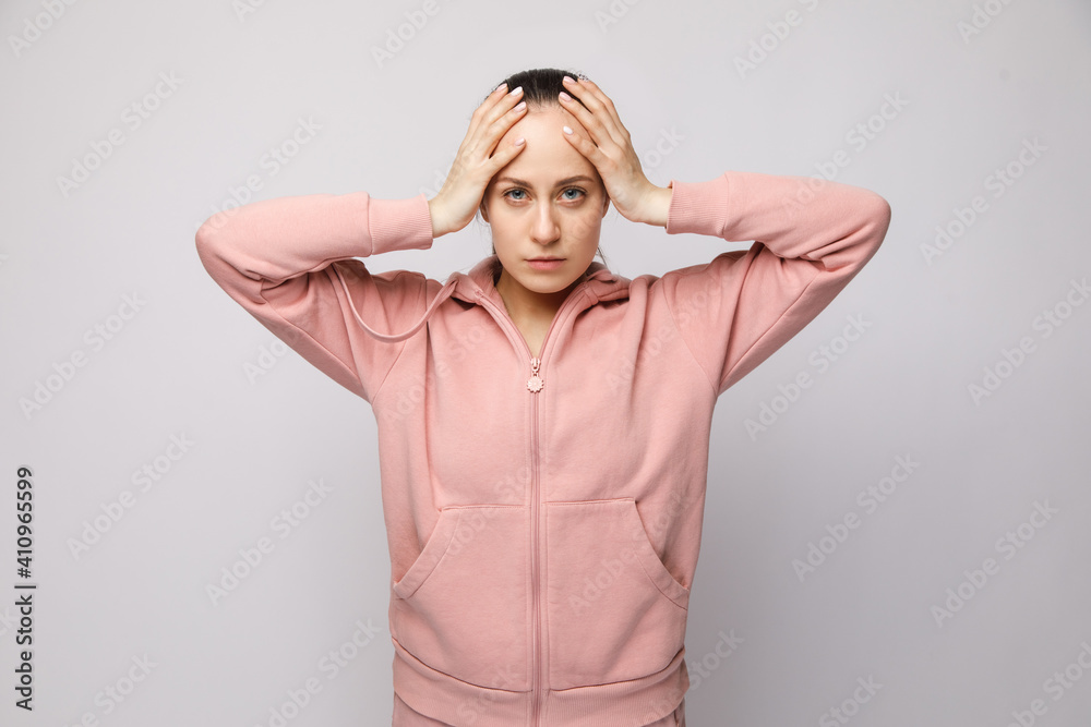 Portrait of a confused, tired young woman holding her head on both sides with both hands, eyes open, isolated on a white background Portrait of a confused, tired young woman holding her head on both sides with both hands, eyes open, isolated on a white background