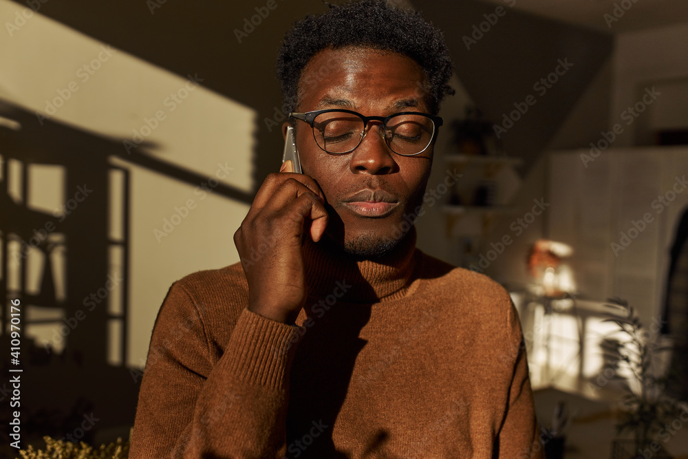 Technology, communication and connection concept. Portrait of handsome calm young dark skinned guy in stylish glasses speaking on mobile with his girlfriend, having peaceful relaxed look, closing eyes Technology, communication and connection concept. Portrait of handsome calm young dark skinned guy in stylish glasses speaking on mobile with his girlfriend, having peaceful relaxed look, closing eyes