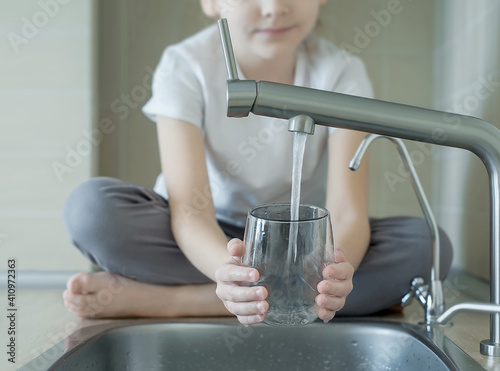 Little girl drinking from water tap or faucet in kitchen. Pouring fresh drink. Healthy lifestyle. Water quality check concept. World water monitoring day. Environmental  pollution problem