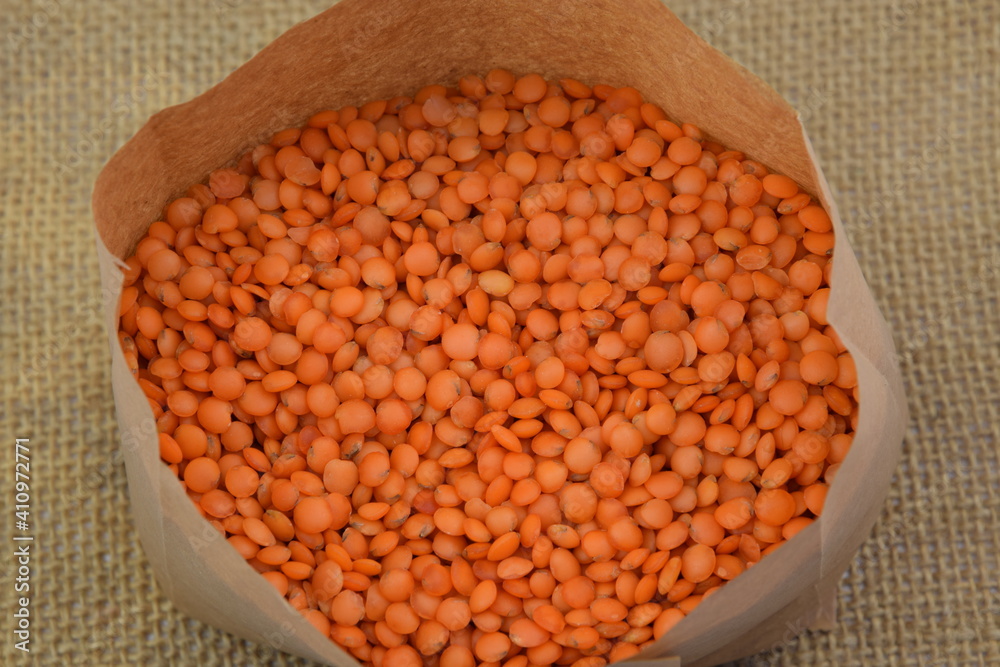 Red lentil in paper bag on jute fabric background closeup Red lentil in paper bag on jute fabric background closeup