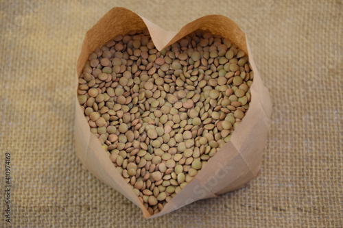 Green lentil in paper bag heart shaped on jute fabric background