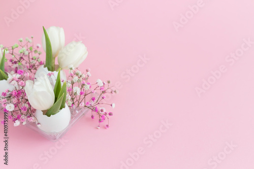 Easter holiday decoration in eggshell white tulips and pink gypsophila and two white eggs on pink pastel background. copy space.