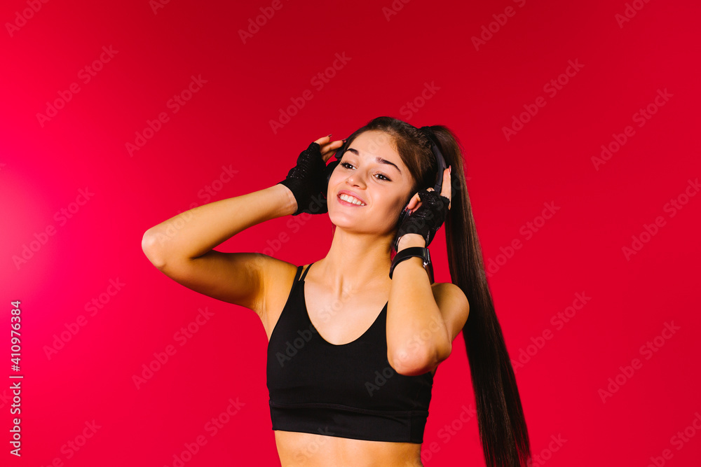 Portrait of a dancing girl wearing big headphones, looking to the side and smiling against a red background with empty side advertising space. Portrait of a dancing girl wearing big headphones, looking to the side and smiling against a red background with empty side advertising space.