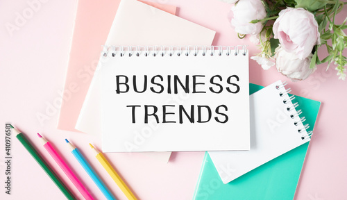Text BUSINESS TRENDS on white paper sheet and brown paper notepad on the table with diagram.