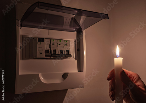 Housewife in complete darkness holding a candle to investigate a home fuse box during a power outage. Blackout, symbolic image.