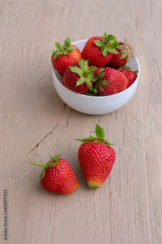 Red ripe strawberries in white bowl on wooden background on daylight. Seasonal berries vertical format
