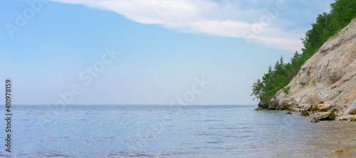 Seascape with crag in green trees in water. Copy space, clear sky