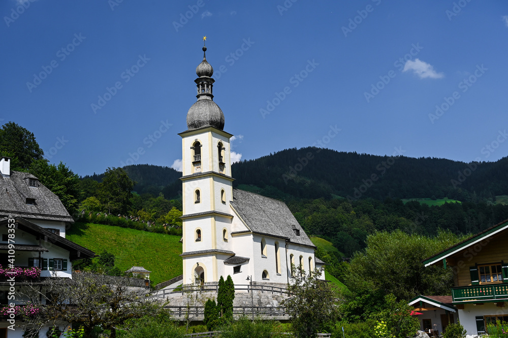 The church of St. Sebastian in the national park Berchtesgaden, Bavaria, Germany. The church is standing in a valley surrounded by forested hills.