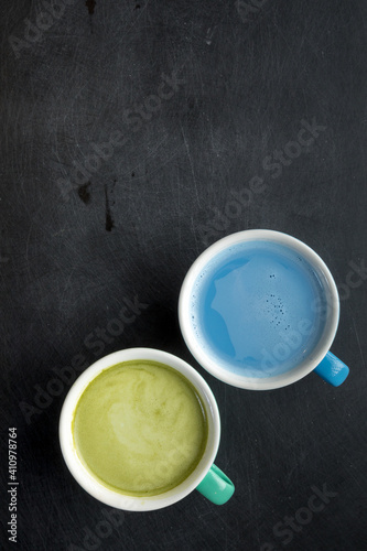 Cup of blue matcha latte and green matcha latte on black scribbled background