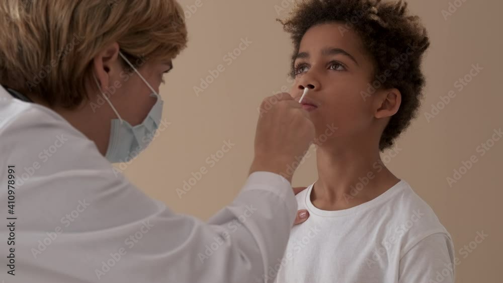 Female practitioner doctor takes nose swab of 10s patient. Little mixed-race boy pass PCR or polymerase chain reaction test for diagnosing of COVID-19 pandemic infection. Medical check up concept Female practitioner doctor takes nose swab of 10s patient. Little mixed-race boy pass PCR or polymerase chain reaction test for diagnosing of COVID-19 pandemic infection. Medical check up concept