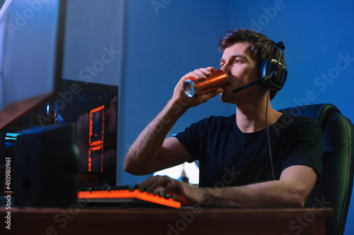 Cyber sport. Professional cybersport player training or playing online video game on his PC late at night, drinking caffeine energy drink to concentrate, focus on game. Team play. Games addiction