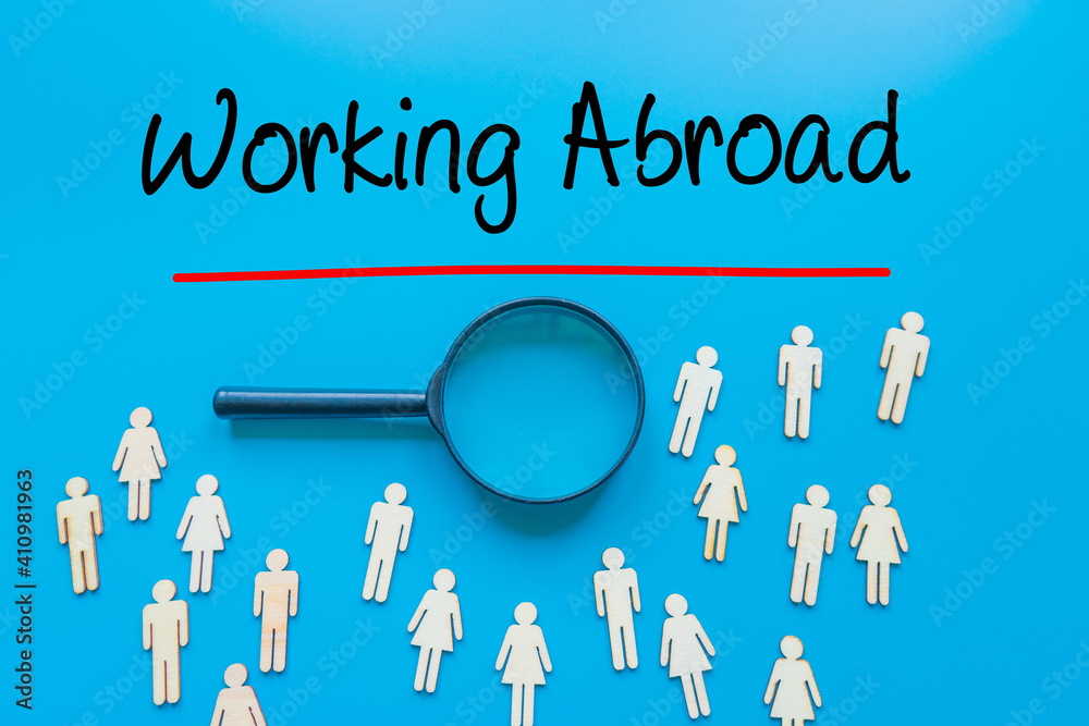 Working Abroad Sign on white paper. Man Hand Holding Paper with text. Isolated on Workers concept, Magnifying glass. Blue. Working Abroad Sign on white paper. Man Hand Holding Paper with text. Isolated on Workers concept, Magnifying glass. Blue.