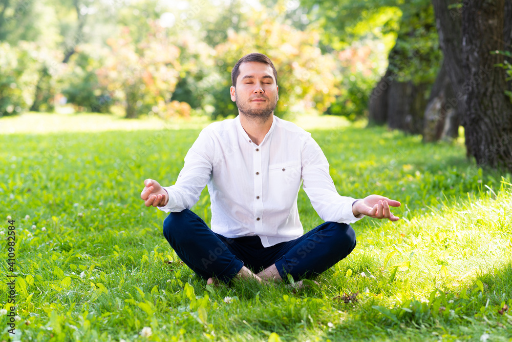Young man meditates in lotus pose on green grass Young man meditates in lotus pose on green grass