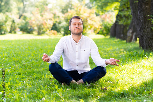 Young man meditates in lotus pose on green grass