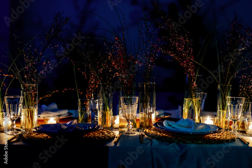 A beautifully decorated table set for a festive candlelit dinner. Glasses, lens flare and dark background. Light from candles. Dinner in the dark. photo