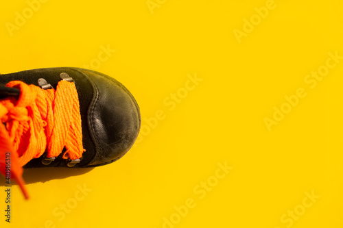 worn children's black shoes with orange laces on a yellow background.