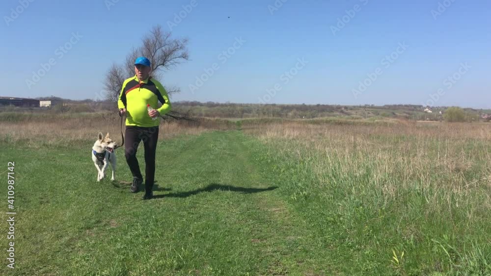 Mature Man running with mixed breed white dog on an earth road at spring season Mature Man running with mixed breed white dog on an earth road at spring season