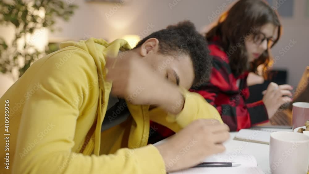 Sleepy mixed-race teenager resting on books while doing homework with a friend