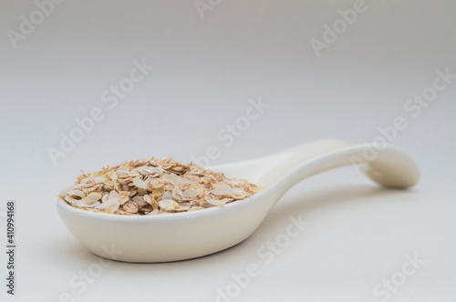 Ceramic white spoon with flakes of various cereals on a white background.