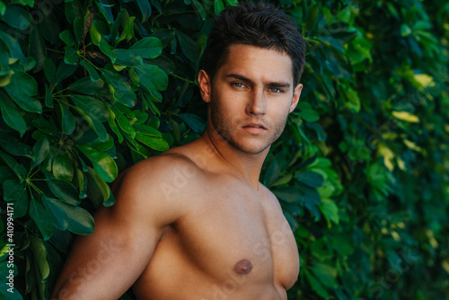 Portrait of handsome man at green background. Sexy shirtless male model in summer garden.