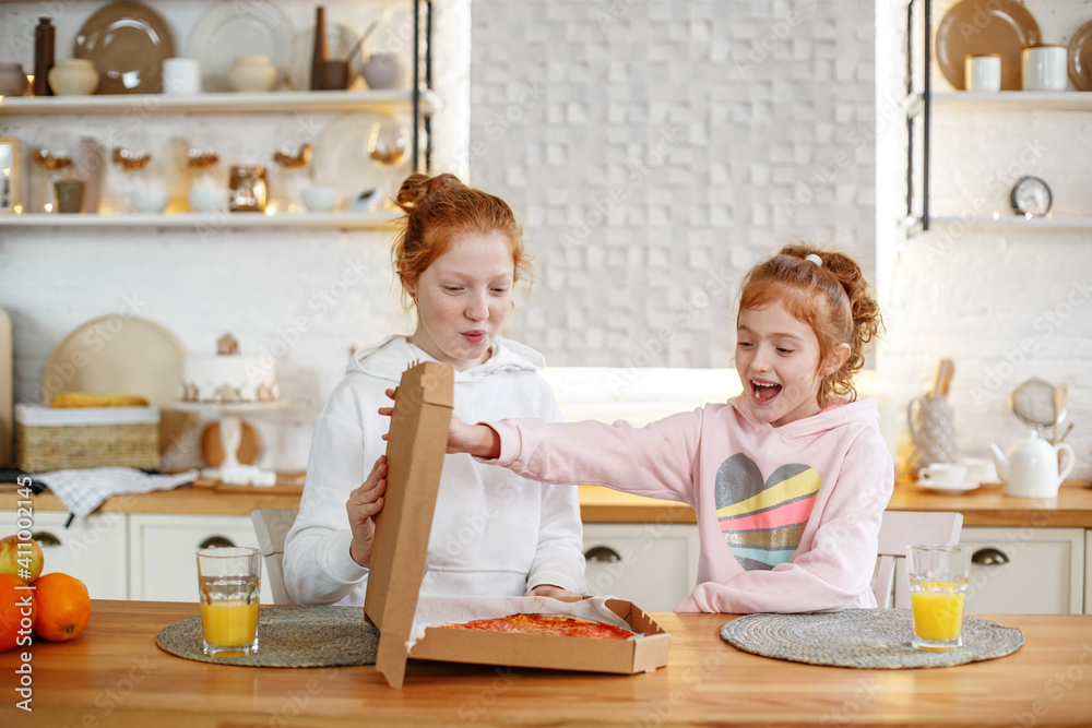 Two young teenage girls with red hair sitting in the kitchen enjoying pizza Two young teenage girls with red hair sitting in the kitchen enjoying pizza
