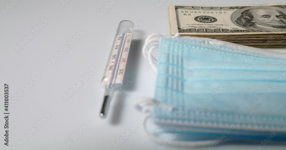 Fever Thermometer, with Clinical Mask and piled up Dollar Bills. 100 Dollar Banknotes, symbol for cost of Health care Fever Thermometer, with Clinical Mask and piled up Dollar Bills. 100 Dollar Banknotes, symbol for cost of Health care