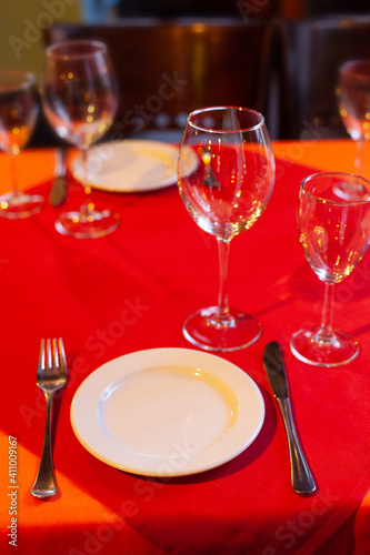 Served table with plate fork knife and wine glass on red and orange tablecloths. Up view.