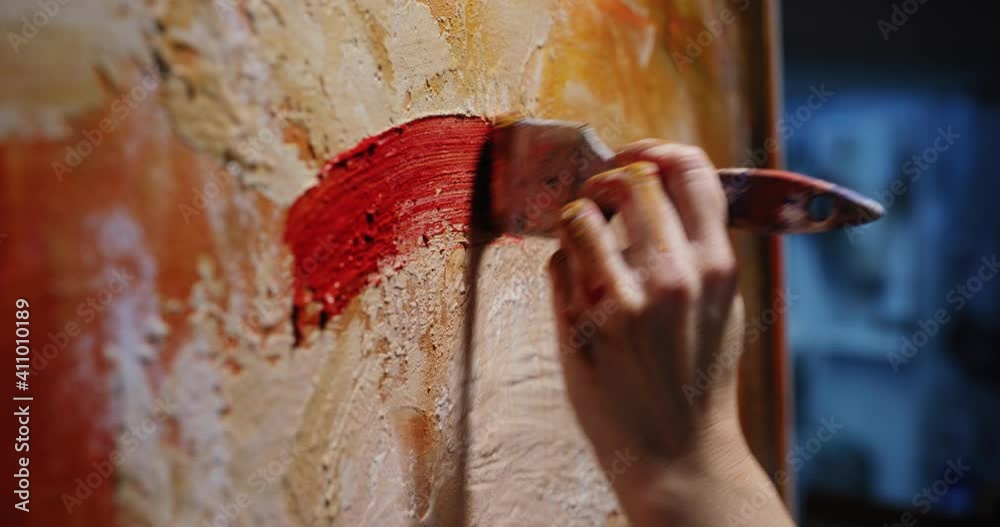 Cinematic macro of female creative artist painter concentrated and inspired painting colorful abstract picture with paint brush and oil colors on canvas while working on new masterpiece for exhibition
