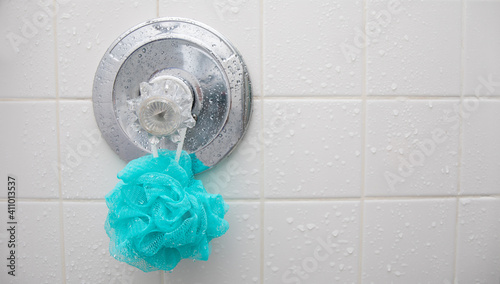 A blue loofah sponge hanging in a wet shower on the temperature guage.