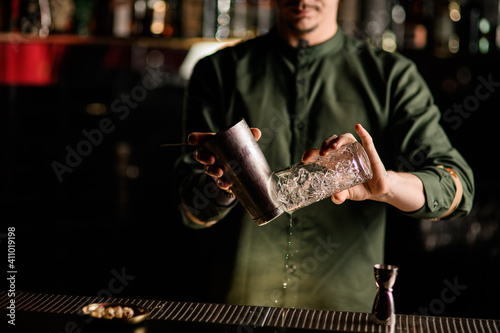 close-up on the hands of man bartender that holds steel shaker cup and crystal glass