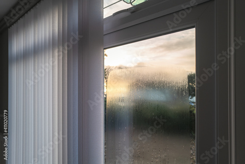 Condensation on the outside of double glazed window glass at sunrise. The window has vertical slat blinds.