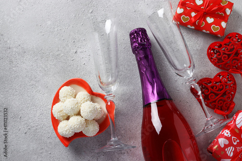 Bottle of champagne, gifts, two glasses and candies on a gray background. Valentine's day concept. Top view photo