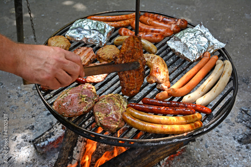 Schwenkgrill mit verschiedenen Fleischwaren Hand wendet Fleisch – Swing grill with various meats hand turns meat
