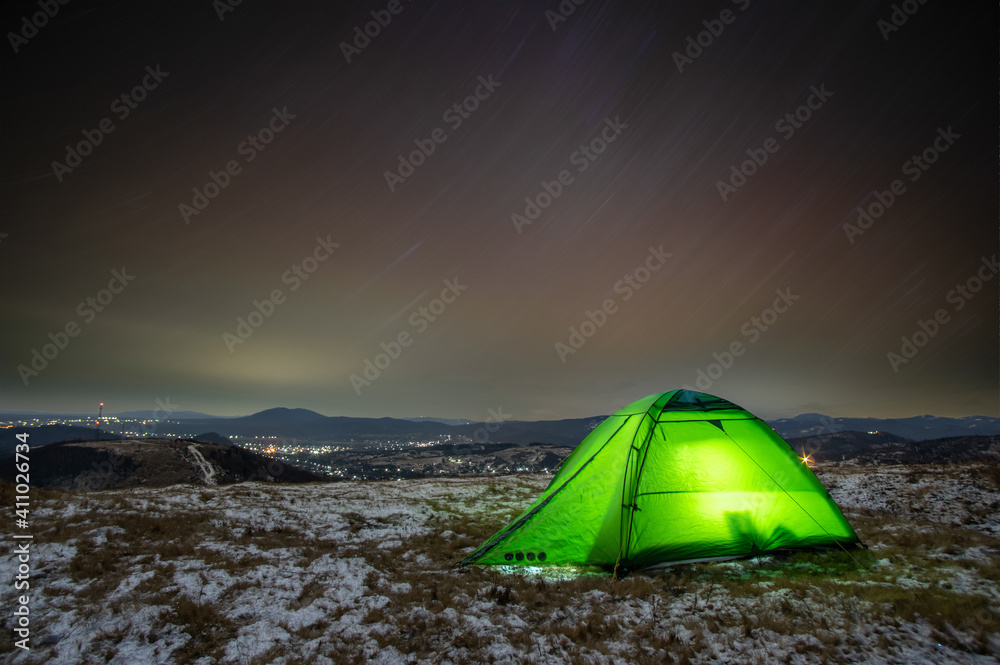 Tent in winter at night on a mountain top with a view of the village
