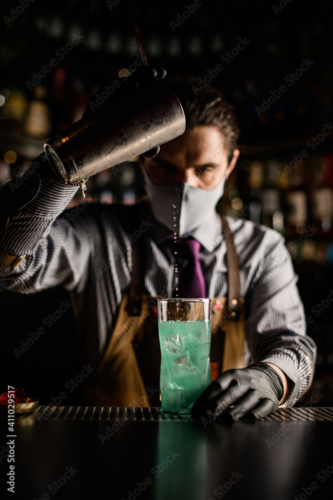 front view of bartender pouring blue cocktail from steel shaker into cup front view of bartender pouring blue cocktail from steel shaker into cup