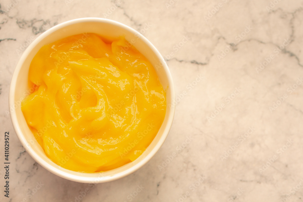 Homemade fresh pudding or tangy lemon curd in a white bowl on marble background.Top view Homemade fresh pudding or tangy lemon curd in a white bowl on marble background.Top view