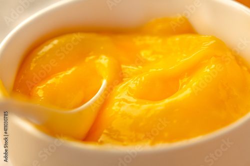 Lemon curd in a sausepan white bowl.Close-up yellow smooth background.Horizontal