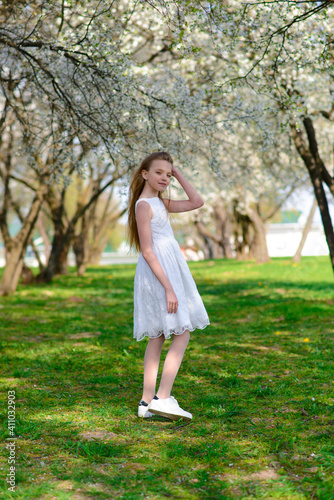 Beautiful blue-eyed girl with blond hair in white dress walking in flower garden,emotional photo.