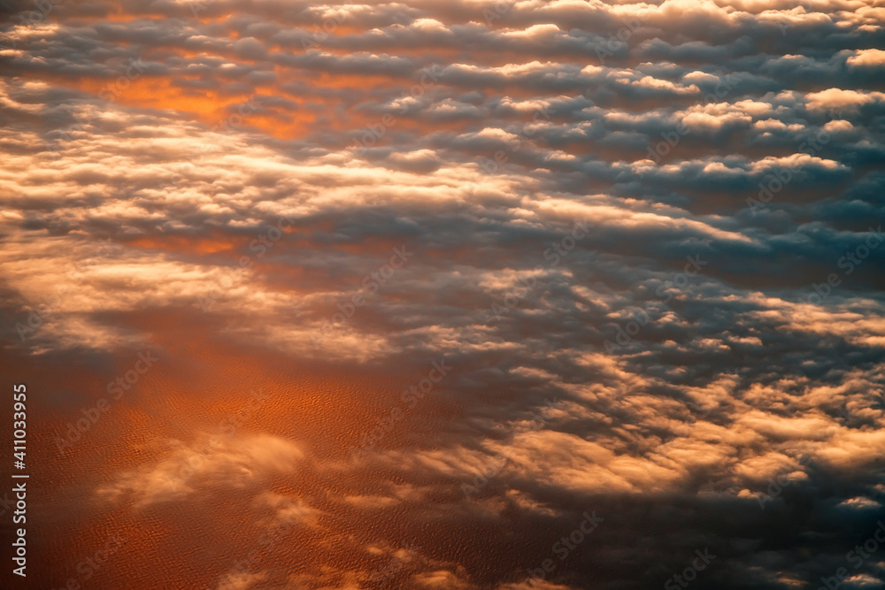 view of the clouds from above from the plane. the sea is colored by the setting sun.
