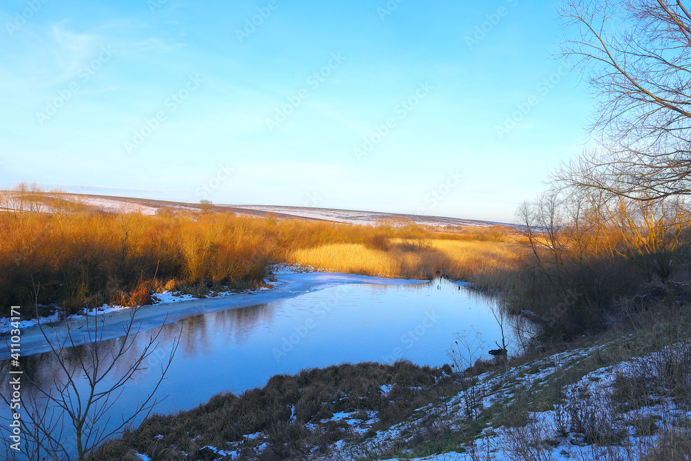 The first snow is a frosty morning. A small river in the grass sprinkled with snow. Golden colors of the morning sun. Rural landscape, Ukraine, Europe.